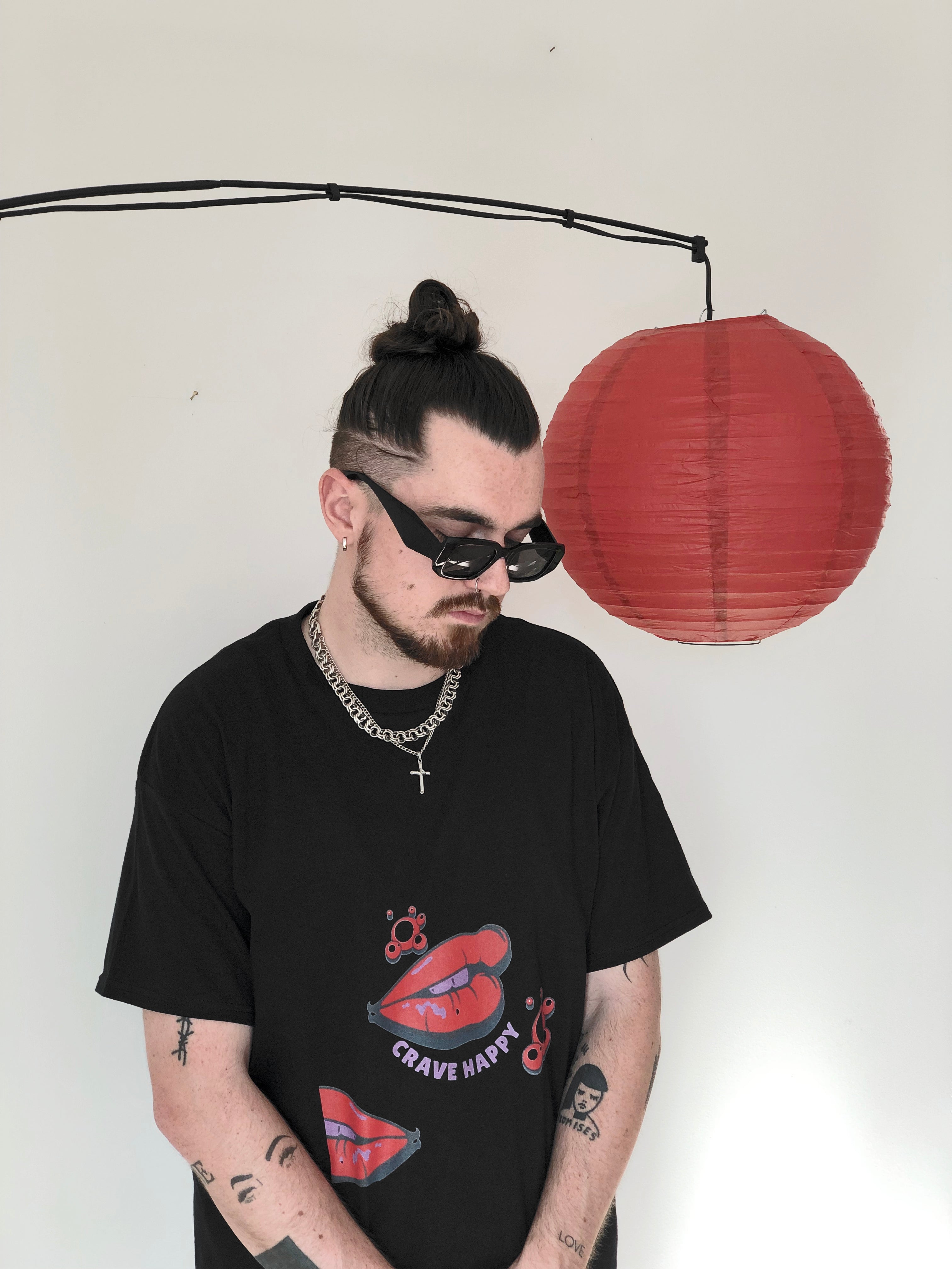 Person wearing a black t-shirt with graphic design, standing against a white wall with a red paper lantern.